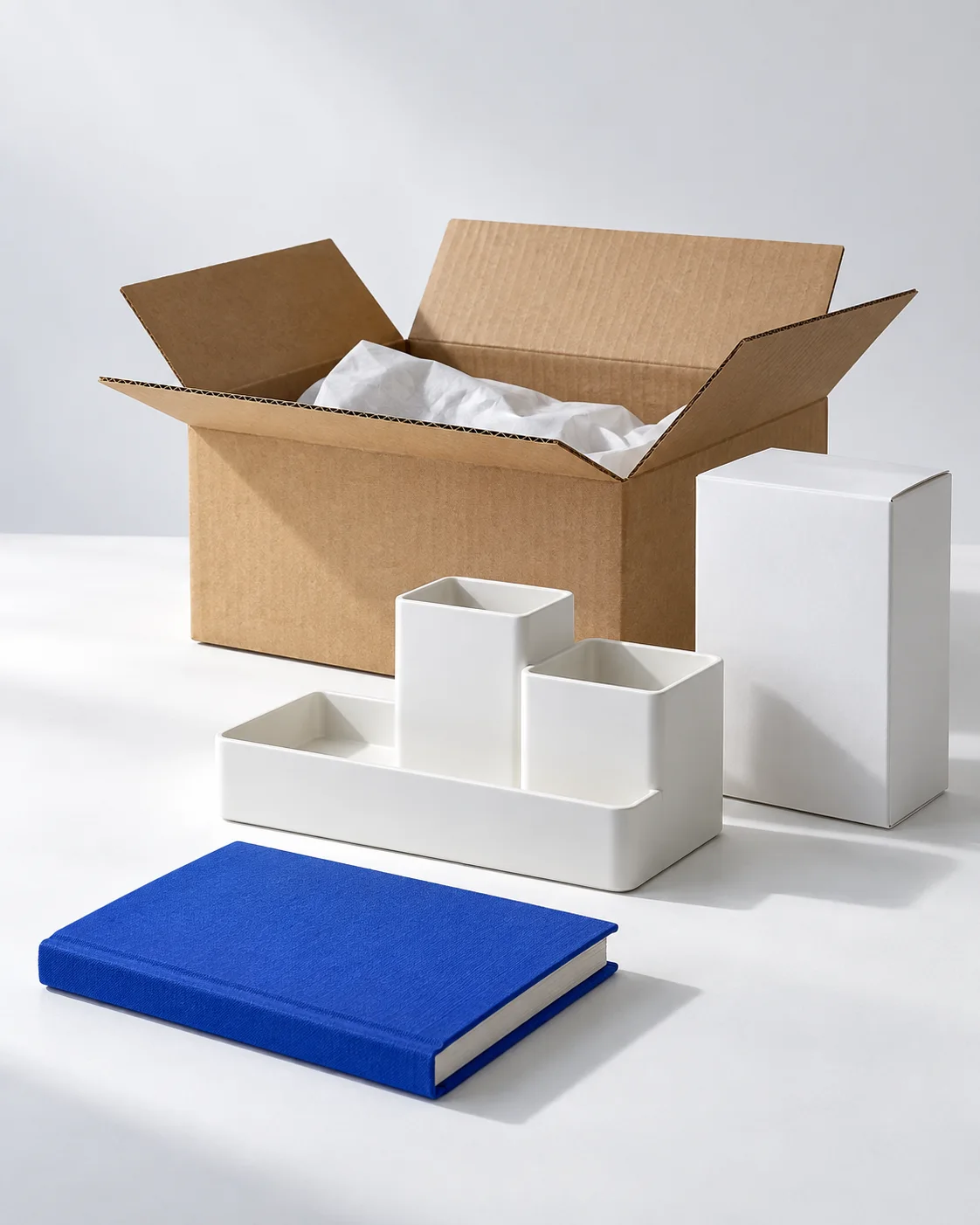 A white desktop organizer, retail packaging, an open shipping box and a cobalt notebook.
